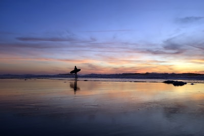A close-up of a surfer wearing lapartisil branded apparel, standing on the beach at sunset.