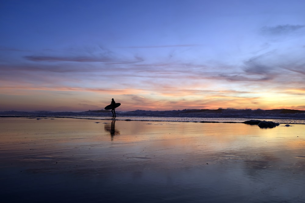 silhouette di persona che cammina in riva al mare durante il tramonto