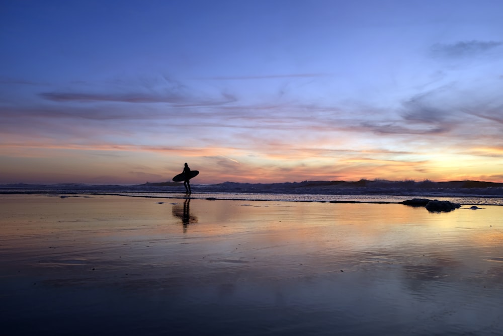 silhouette of person walking on seashore during sunset