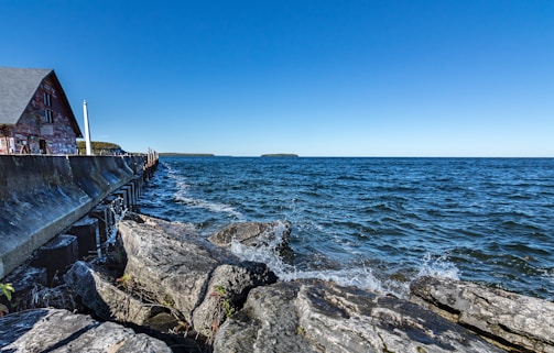 A sturdy seawall being built along a rocky shoreline under a clear blue sky.