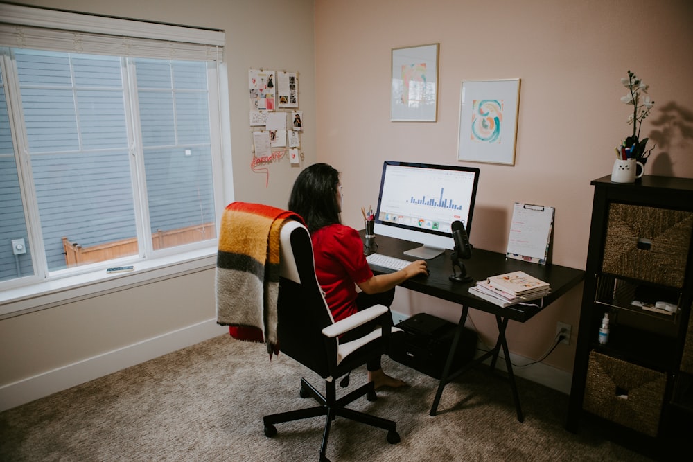 woman in red shirt sitting on chair using computer