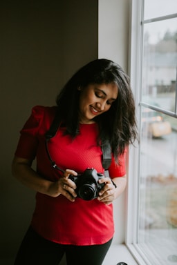 A friendly real estate agent holding a camera, smiling warmly in a bright, modern home.