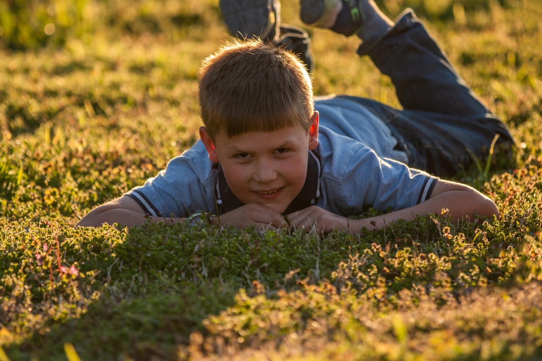 boy in blue jacket lying on green grass field during daytime