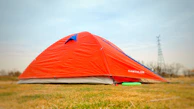 A bright orange tent pitched on a grassy campsite under a clear blue sky.