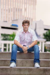 man in white polo shirt and blue denim jeans sitting on concrete bench during daytime