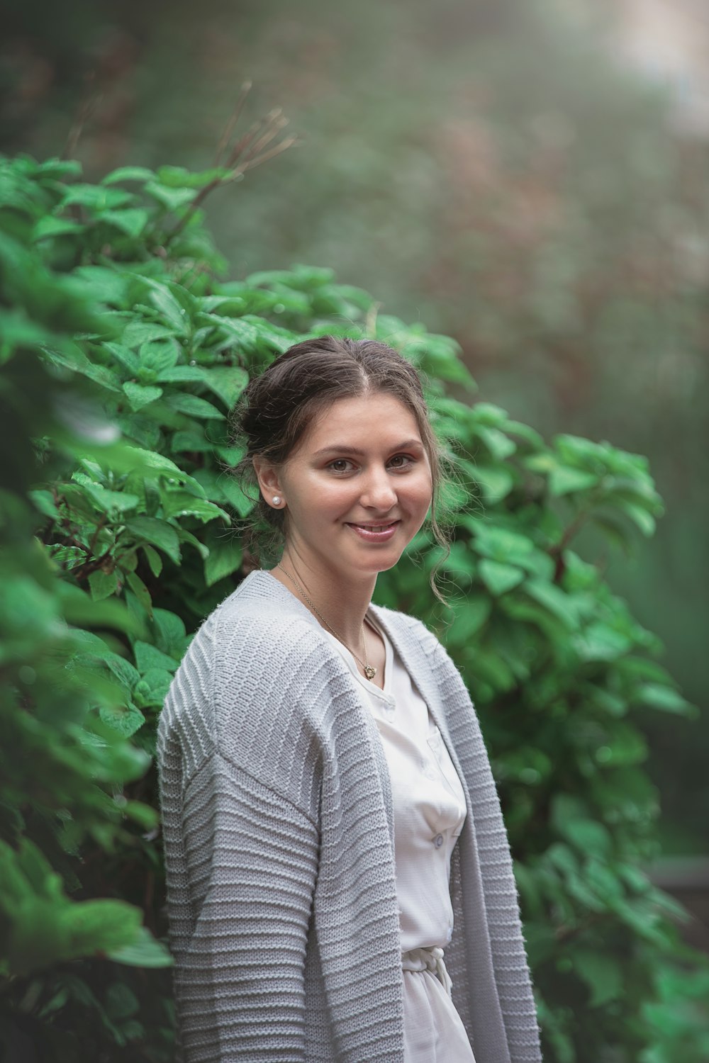 woman in gray and white striped cardigan standing near green plants during daytime