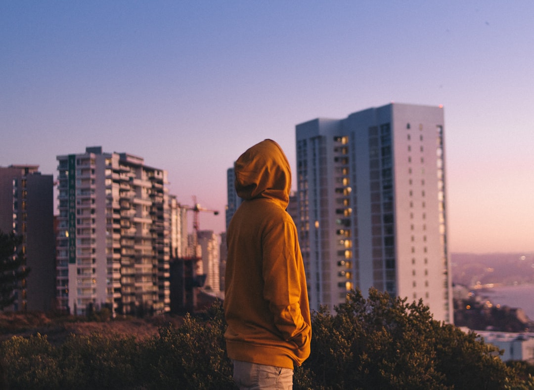 man in yellow hoodie standing in front of city buildings during daytime