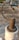 A close-up of a rusty metal valve lever attached to a white plastic pipe. The metal has a rough texture and a curved handle ending in a solid piece. The background is blurred and appears to be an outdoor setting, possibly a rooftop or concrete surface.