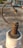 A close-up of a rusty metal valve lever attached to a white plastic pipe. The metal has a rough texture and a curved handle ending in a solid piece. The background is blurred and appears to be an outdoor setting, possibly a rooftop or concrete surface.