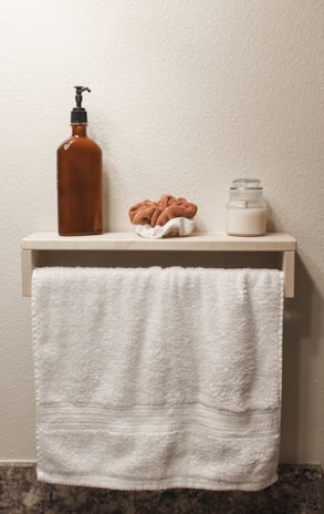 A neatly arranged bathroom shelf with soft towels, a glass jar of bath salts, and a scented candle glowing warmly.
