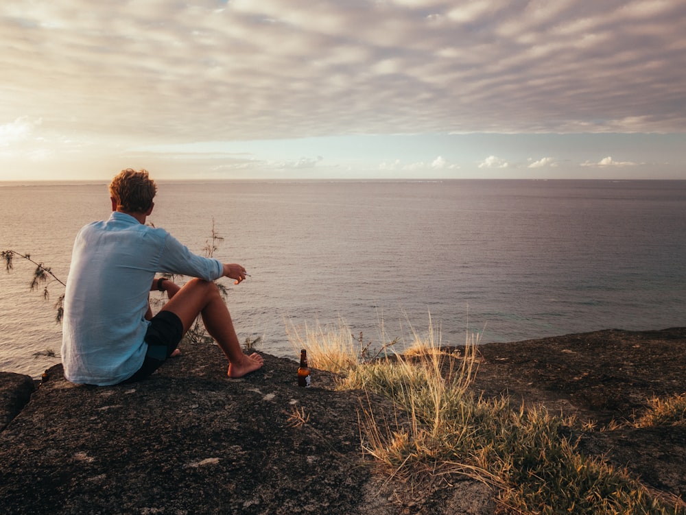 man in white t-shirt sitting on rock near sea during daytime