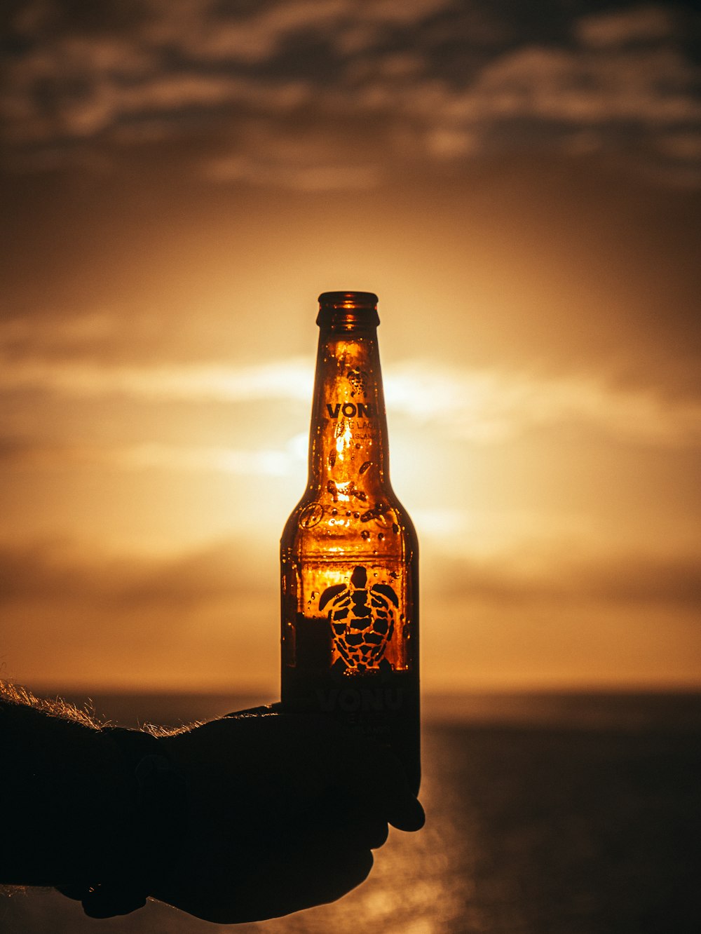 garrafa de vidro marrom na rocha preta durante o pôr do sol