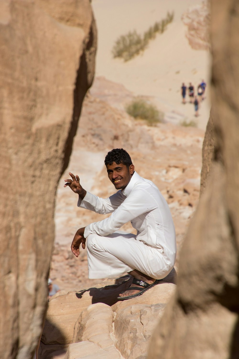 man in white dress shirt and gray pants sitting on brown rock during daytime