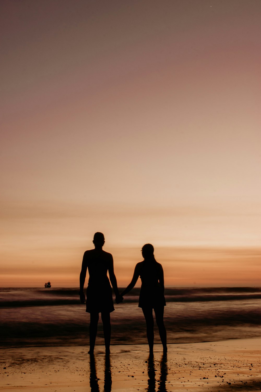 夕暮れ時の海岸に立つ2人の男女のシルエット