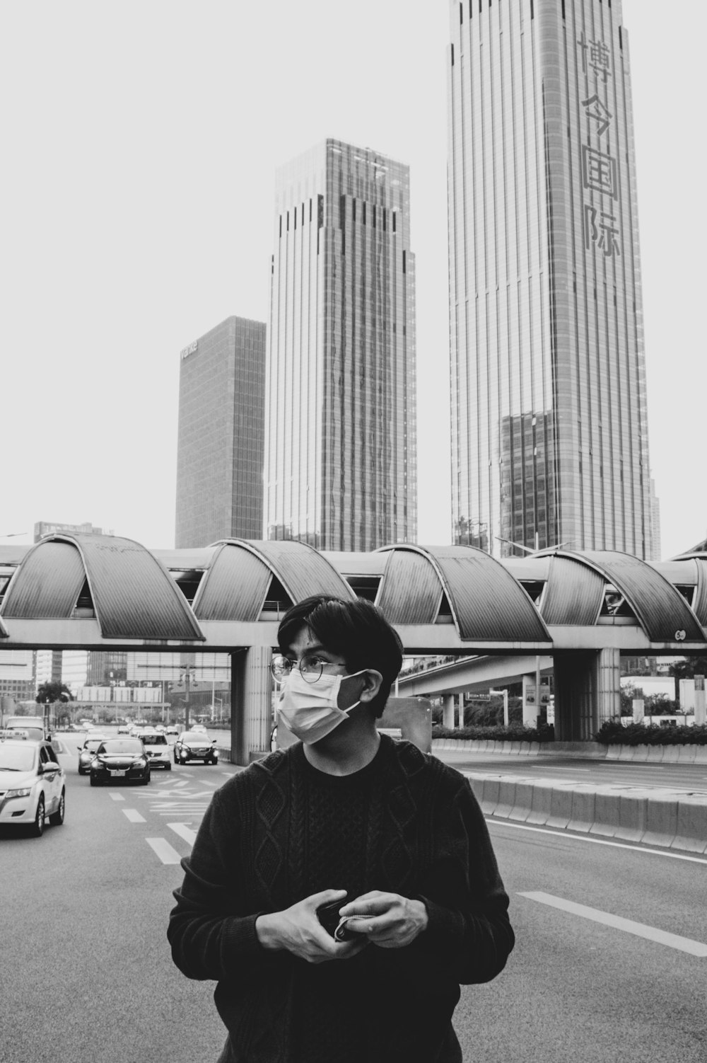 grayscale photo of man in black jacket standing near building