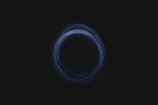 A circular pattern, resembling a vortex or swirling effect, is depicted against a dark background. The circle is composed of thin, semi-transparent lines with varying shades of blue.