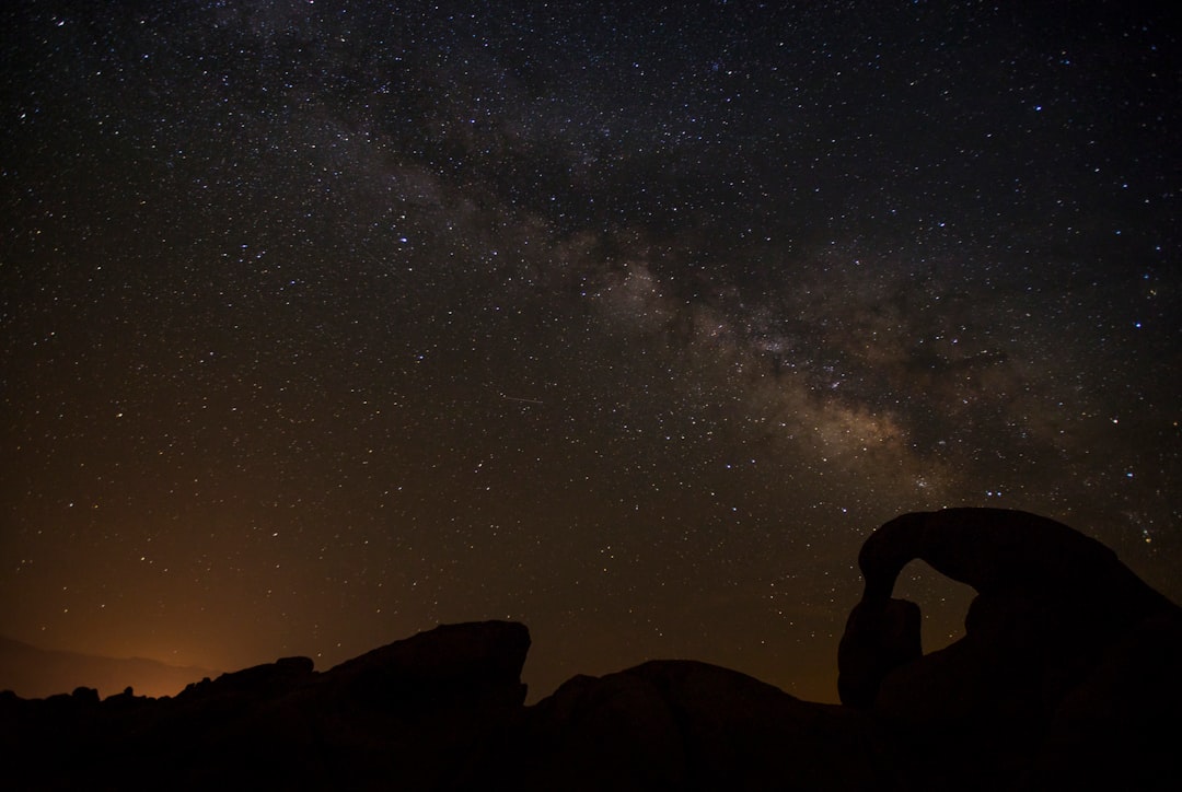 silhouette of man standing on rock formation under starry night
