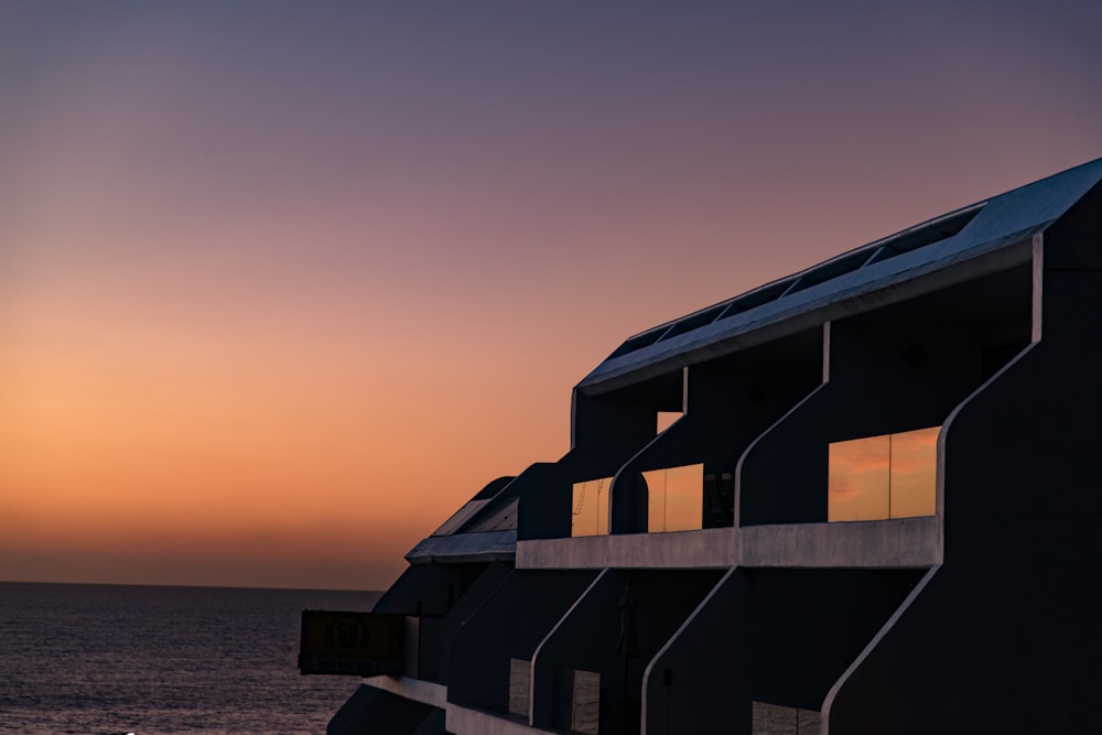 silhouette of house near body of water during sunset