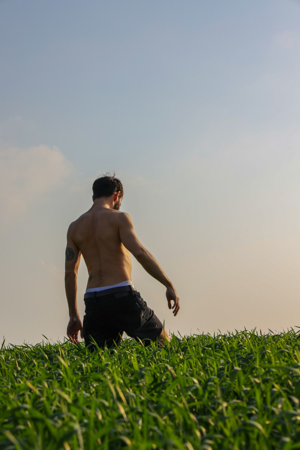topless man in black shorts sitting on green grass field during daytime
