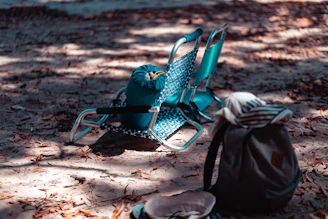 A folded olive green picnic mat resting on sandy ground beside a compact backpack.