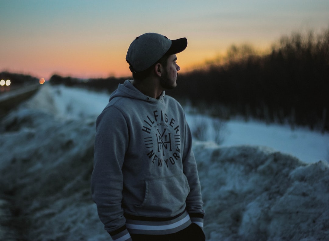 man in gray hoodie and black knit cap standing on snow covered ground during daytime