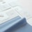 The image displays several fabric samples and garment tags on a surface. The fabric is light blue with a smooth texture, while the tags are made of white paper with printed text and icons. The text includes laundry symbols and manufacturing information.