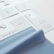 The image displays several fabric samples and garment tags on a surface. The fabric is light blue with a smooth texture, while the tags are made of white paper with printed text and icons. The text includes laundry symbols and manufacturing information.