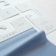 The image displays several fabric samples and garment tags on a surface. The fabric is light blue with a smooth texture, while the tags are made of white paper with printed text and icons. The text includes laundry symbols and manufacturing information.