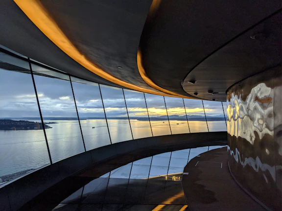 Wide-angle view of a luxury residence’s open-plan interior with soft light gray walls and large glass windows overlooking the sea.