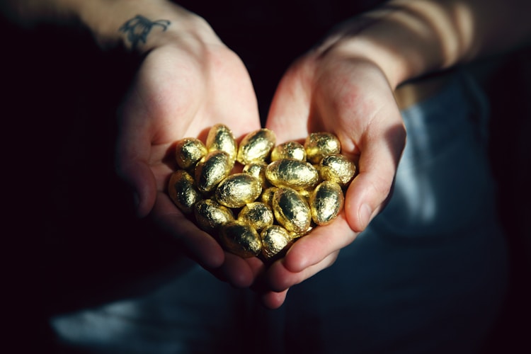 A person holding small round gold objects, demonstrating the tactile reality of gold purity assessment that has been practiced for millennia