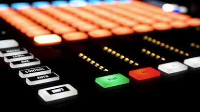 A control panel with various buttons and illuminated indicators. The buttons include labels such as PLAY, REC, AUTO, and CONTROL. The PLAY button is green, and the REC button is red. There are also a series of small yellow lights arranged in rows.