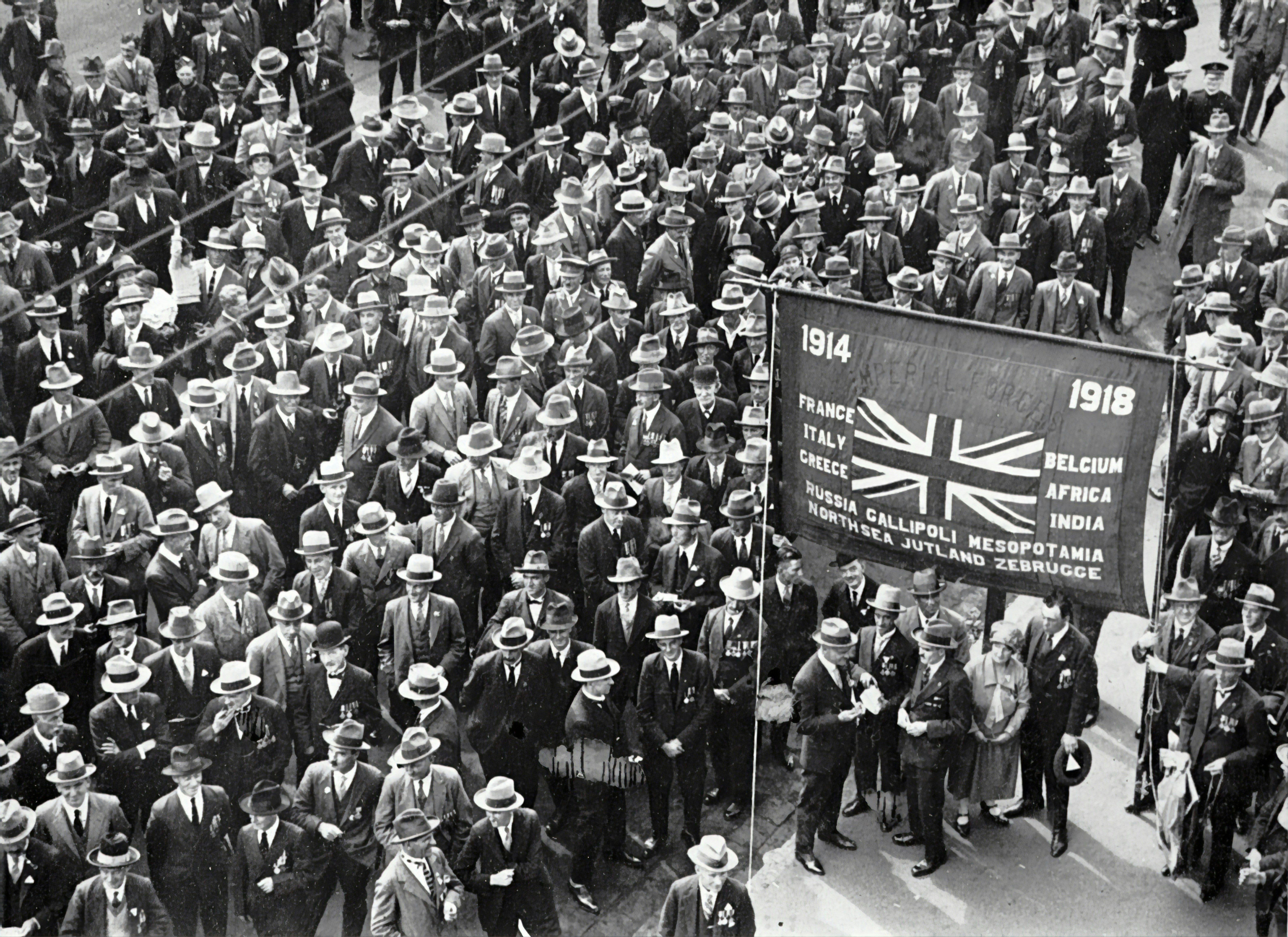 Crowds at the Anzac Day march. In the foreground is a banner proclaiming the engagements of Empire Forces (?) between 1914 and 1918. 
