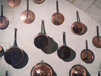 Close-up of shiny aluminum frying pans and milk pans arranged neatly on a wooden surface.