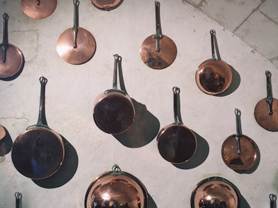 Close-up of shiny aluminum frying pans and milk pans arranged neatly on a wooden surface.