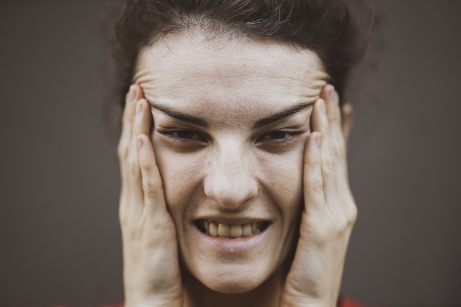 Woman pressing both hands to her jaw and temples in discomfort, a typical presentation of TMJ pain