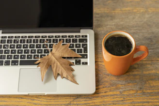 macbook pro beside orange ceramic mug with coffee