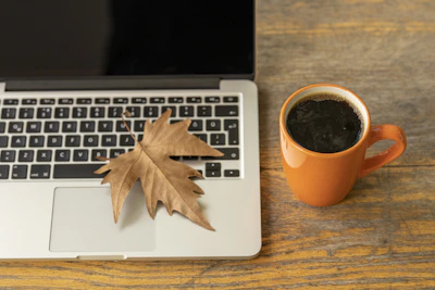 macbook pro beside orange ceramic mug with coffee