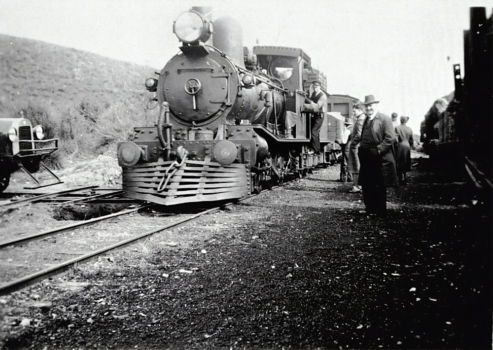 grayscale photo of people standing beside train