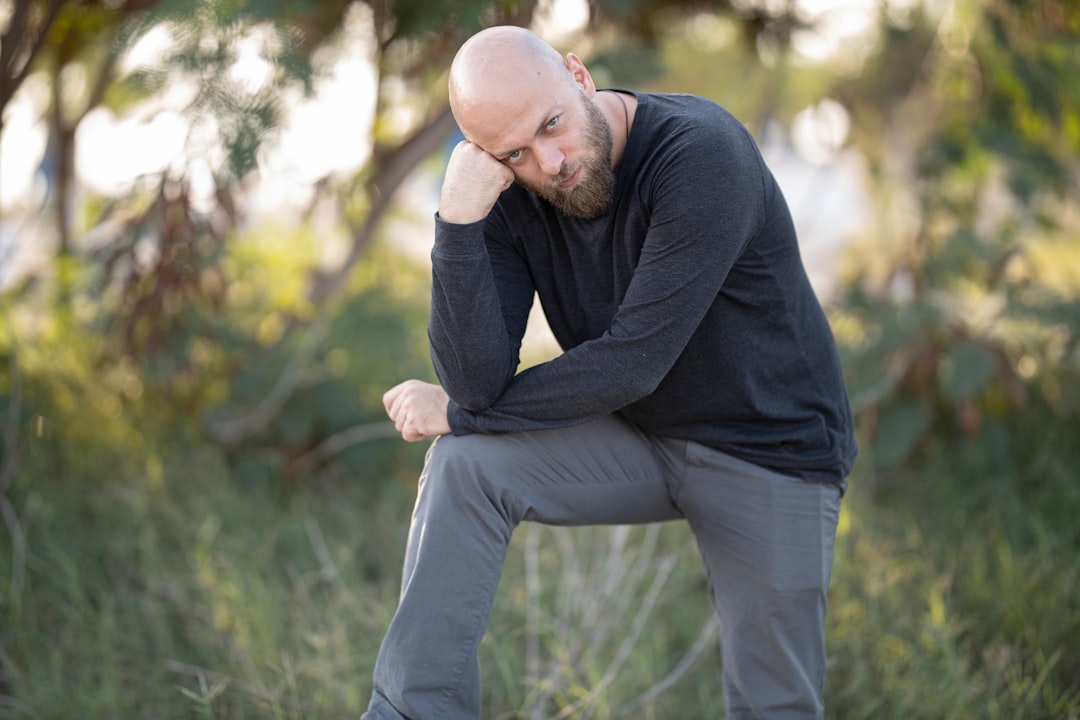 man in black long sleeve shirt and gray pants sitting on green grass during daytime