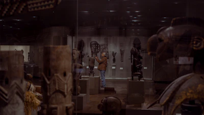 A wide shot of a museum-style exhibit featuring several wooden sculptures under soft gallery lighting.