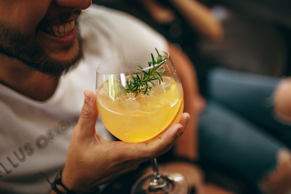 man in white shirt holding clear wine glass with yellow liquid