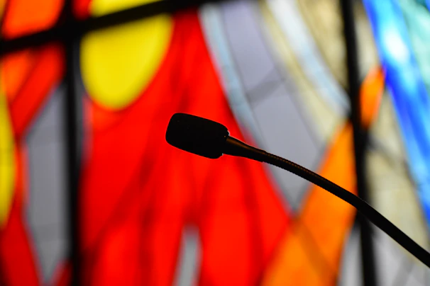 A vintage microphone set against stained glass windows glowing with warm colors.