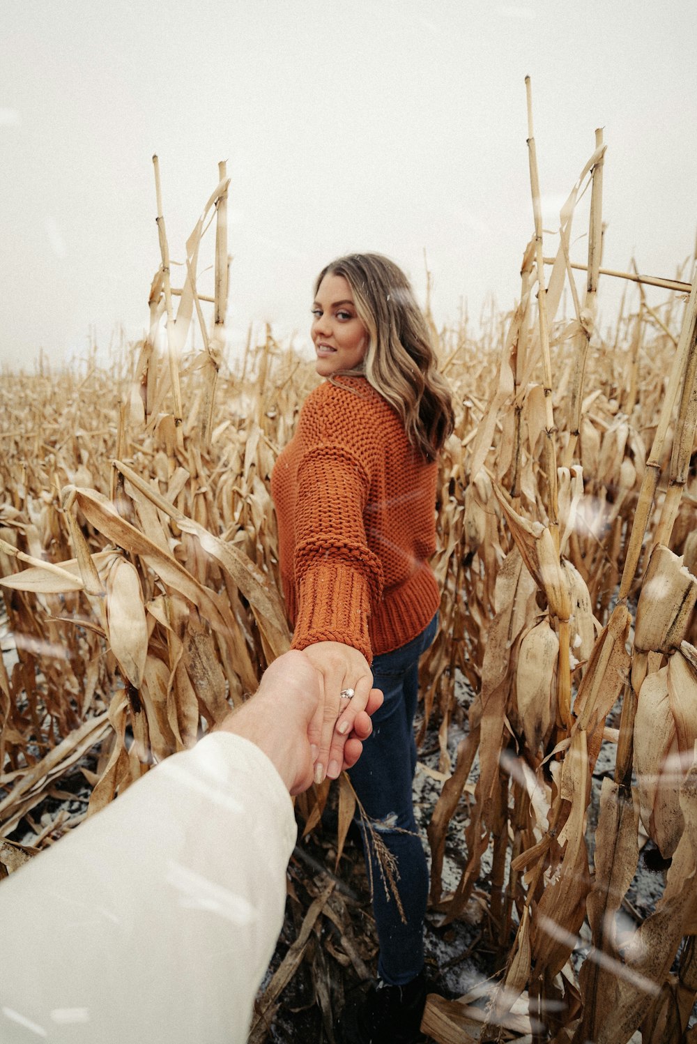 woman in red knit sweater and blue denim jeans standing on wheat field during daytime