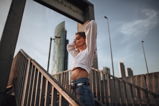 woman in white long sleeve shirt and blue denim jeans leaning on brown wooden railings during