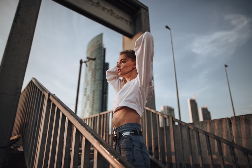 woman in white long sleeve shirt and blue denim jeans leaning on brown wooden railings during