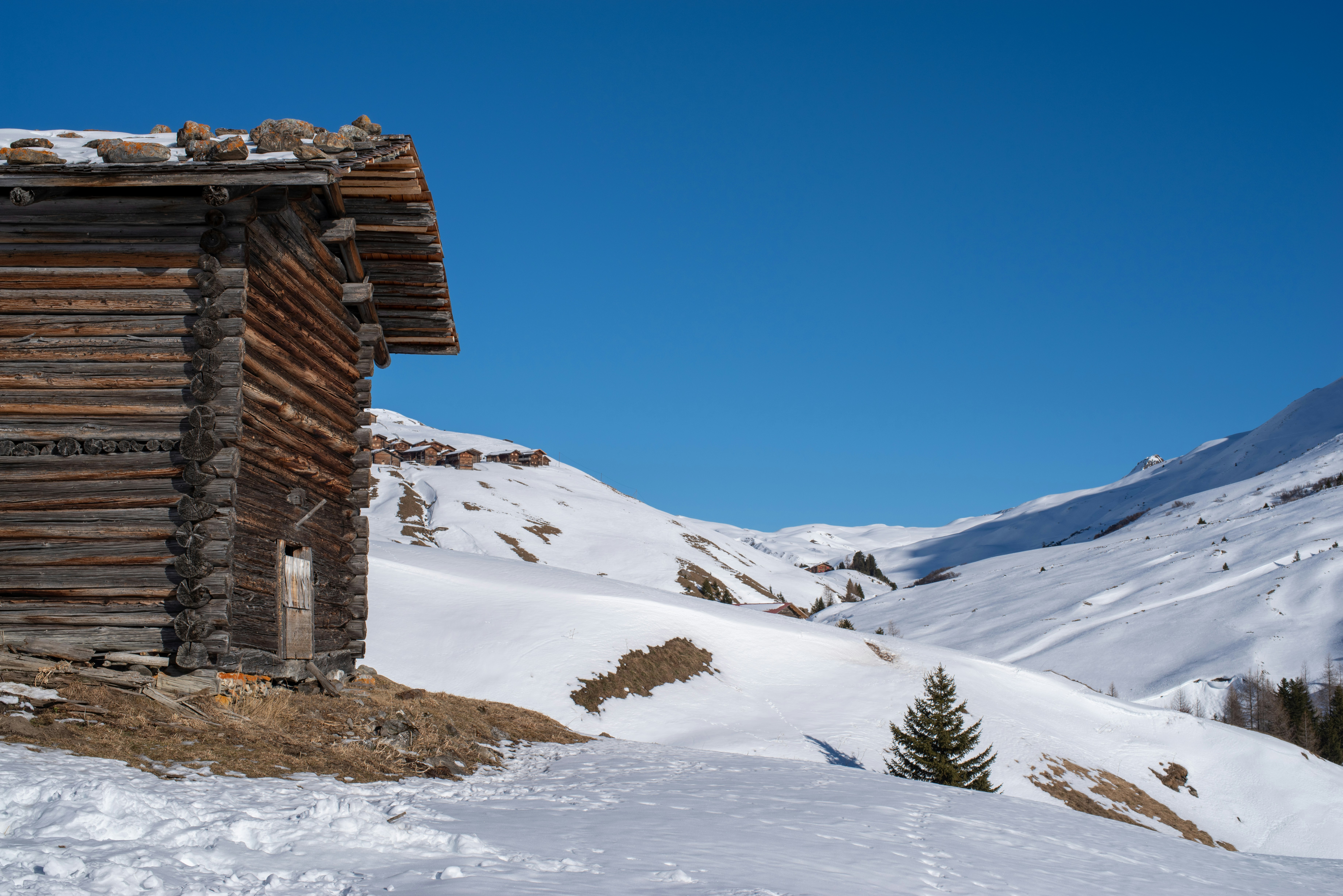 brown wooden house on snow covered ground under blue sky during daytime