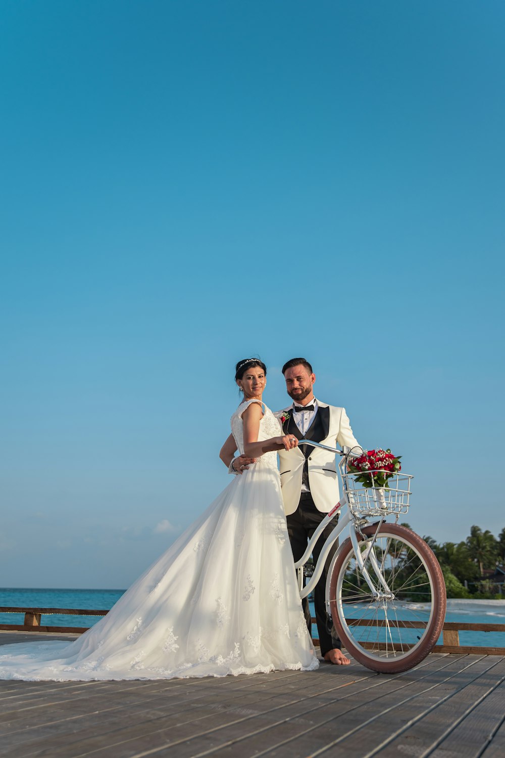 uomo e donna in abito da sposa in bicicletta sulla spiaggia durante il giorno