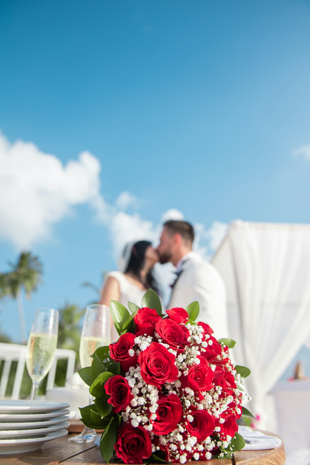 man in white suit holding red rose bouquet