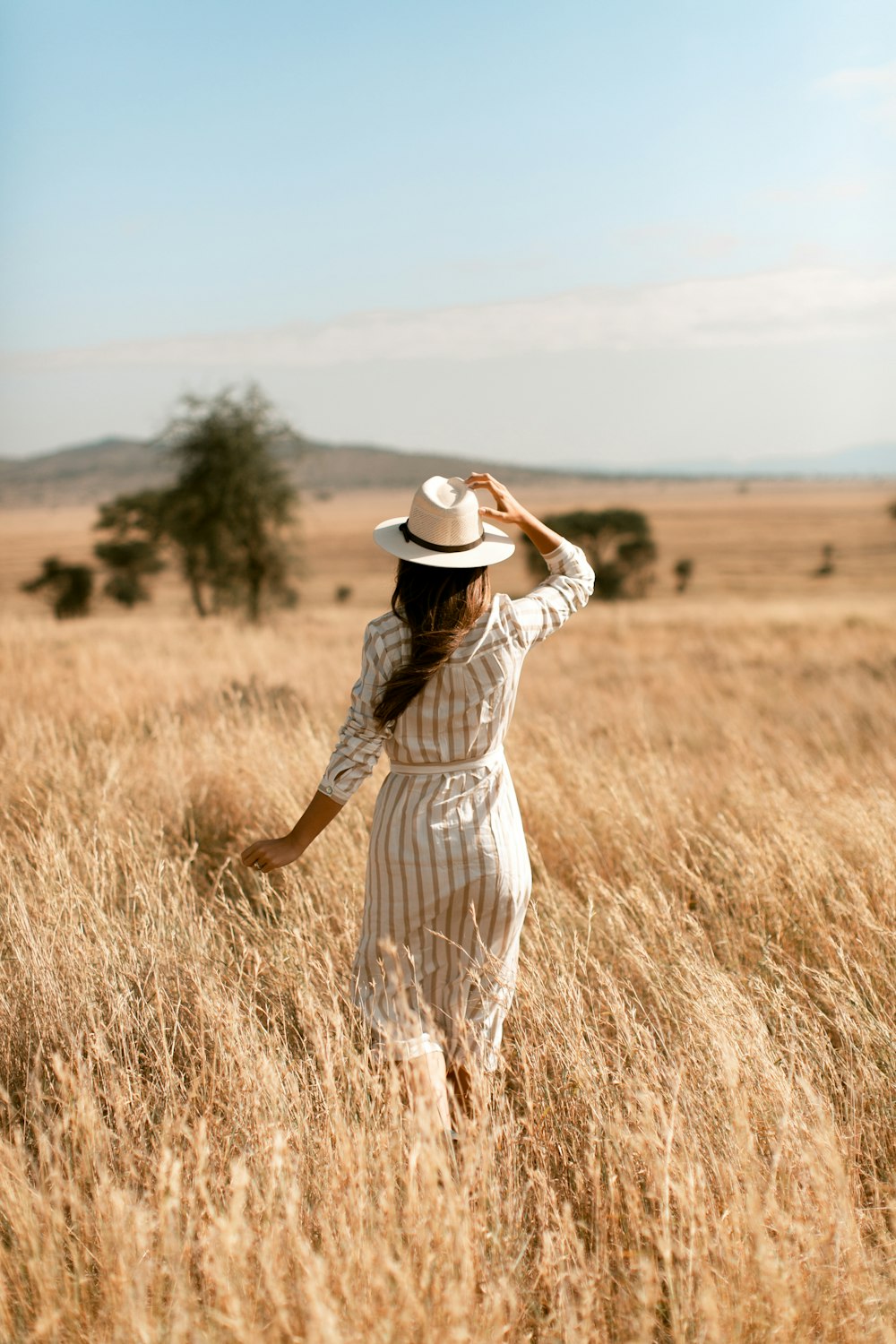 woman in white and black stripe dress wearing brown cowboy hat standing on brown grass field