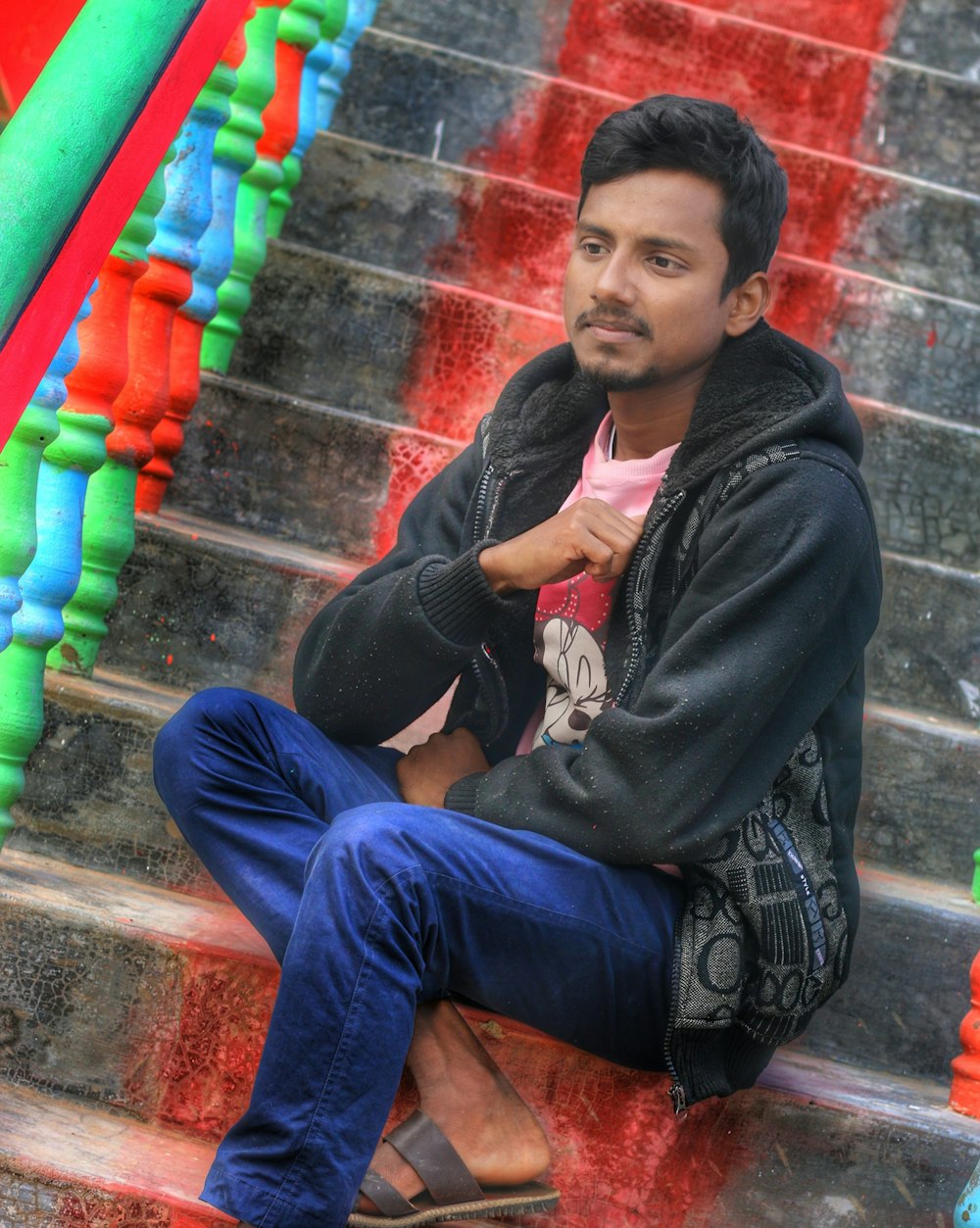 boy in black jacket and blue denim jeans sitting on concrete stairs